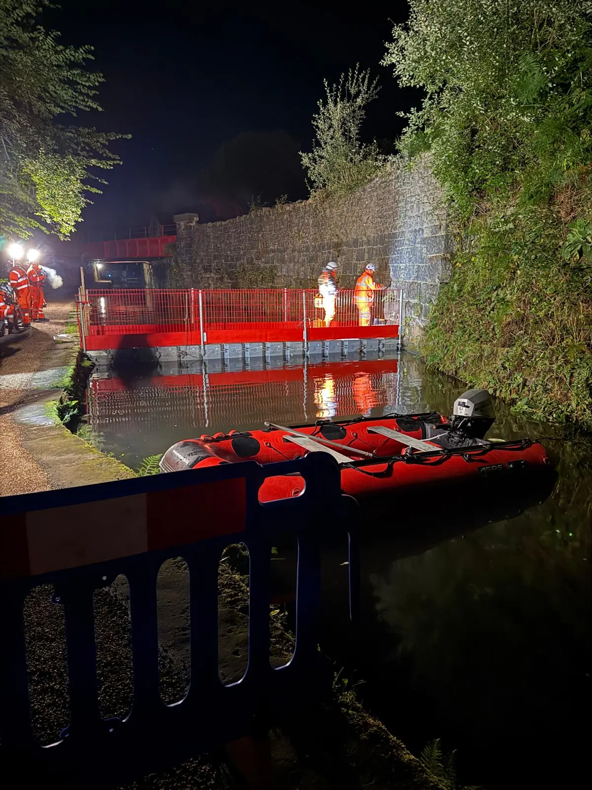 CRM operatives working from a protected floating walkway beneath a canal bridge at night