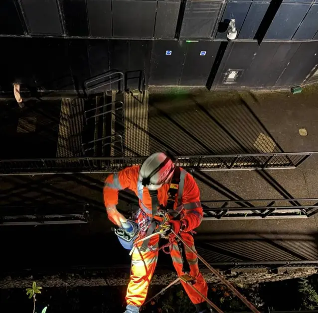 IRATA rope-access technician working beside rail infrastructure at night