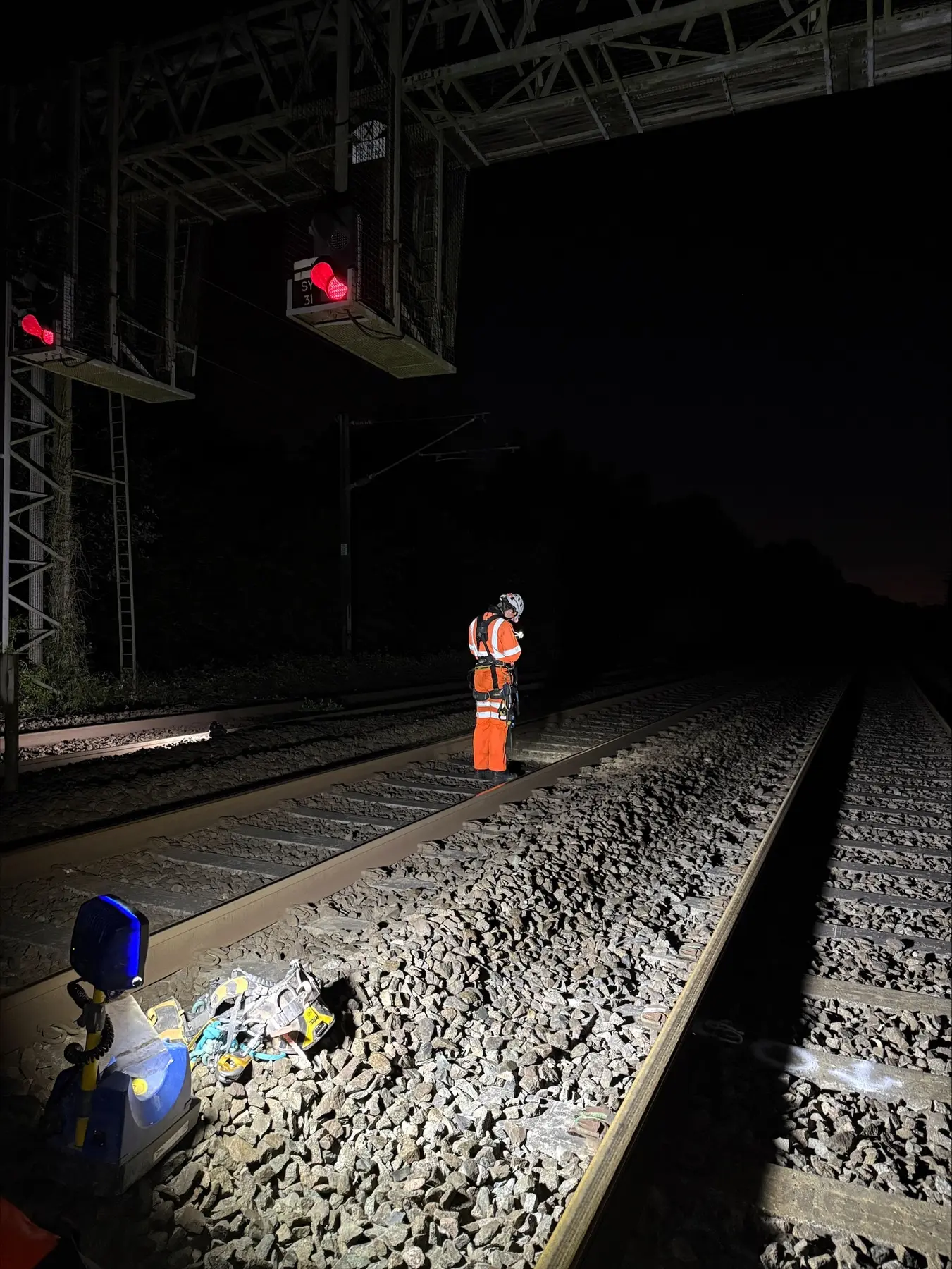 Rope-access technician preparing equipment on railway infrastructure during a night shift